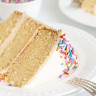 A slice of vanilla cake recipe on a white plate with fork leaning on the plates