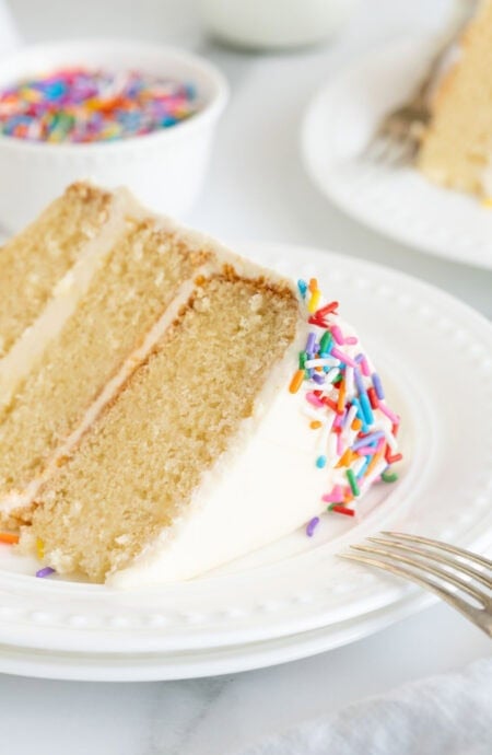 A slice of vanilla cake recipe on a white plate with fork leaning on the plates