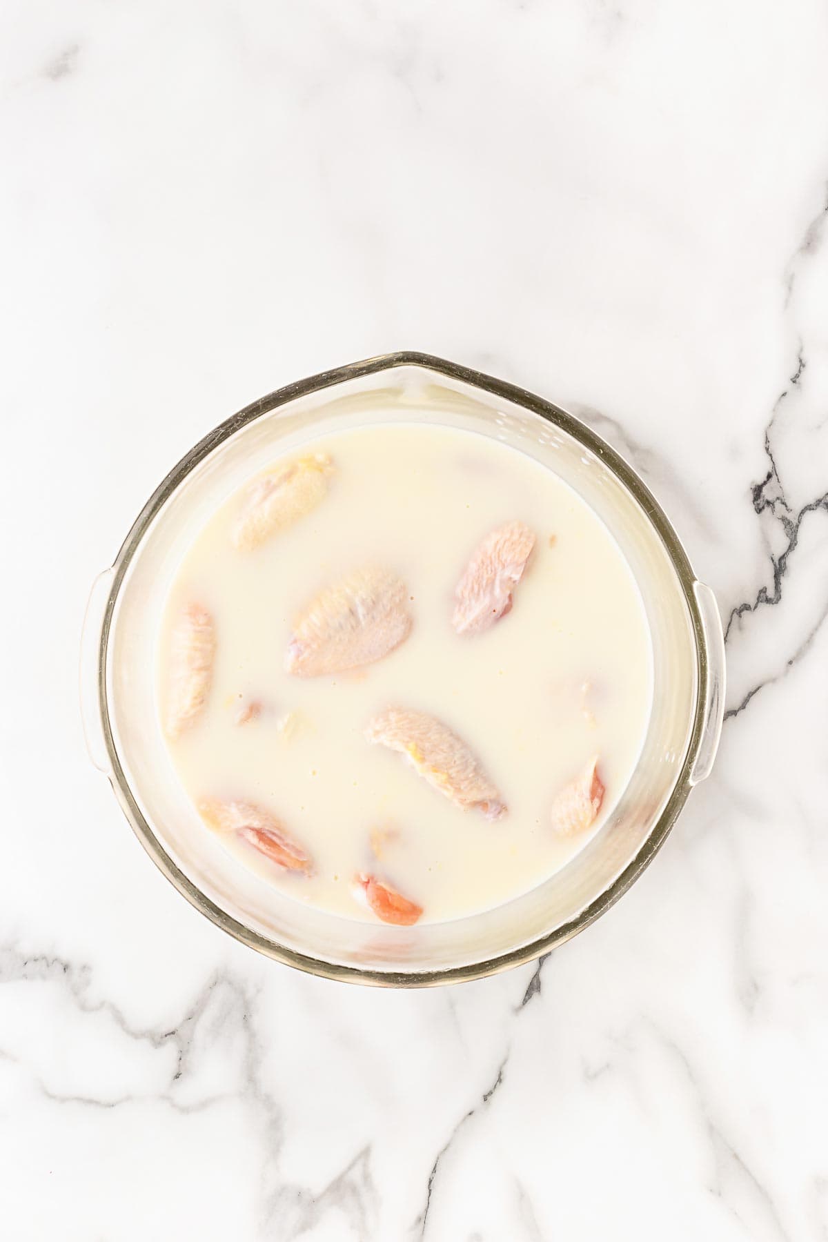 Raw chicken wings soaking in buttermilk marinade