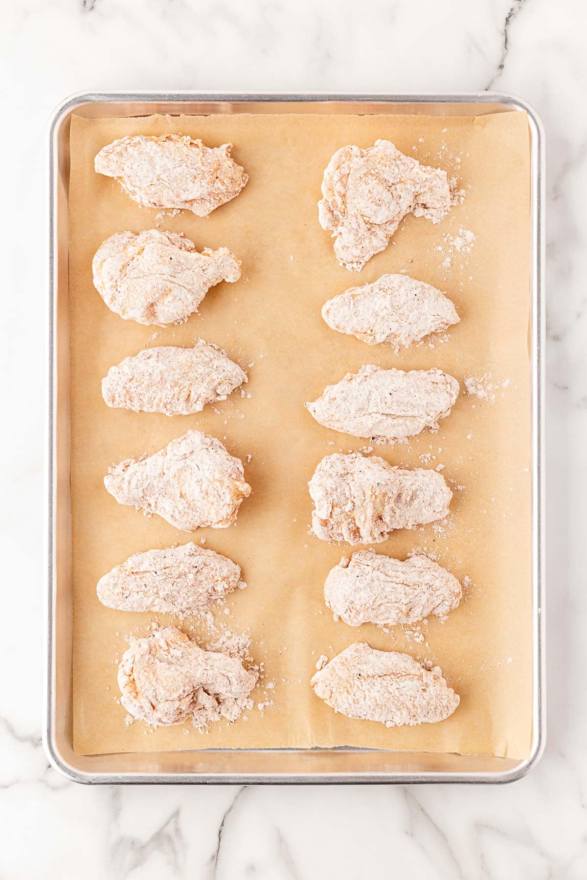 Breaded chicken wings arranged on parchment-lined baking sheet