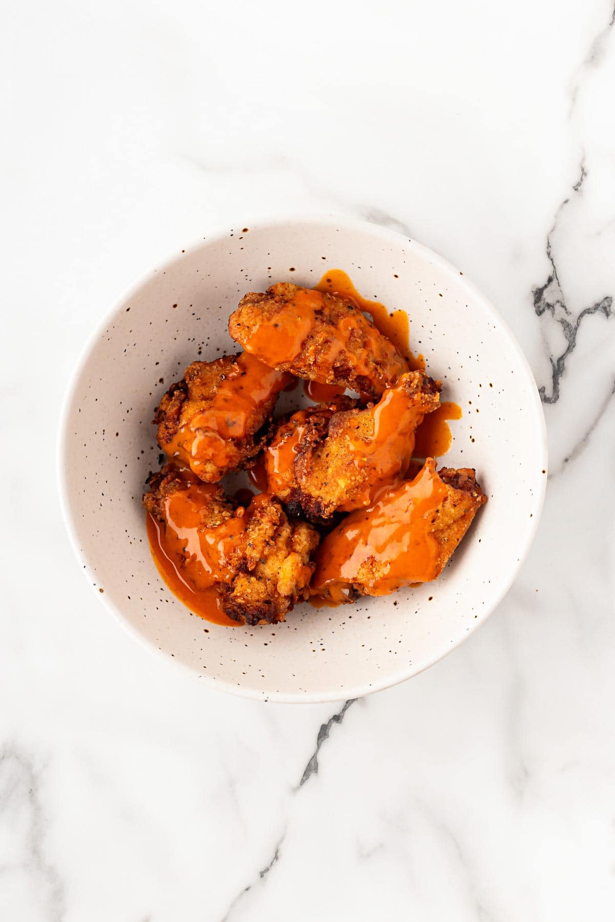 Fried wings tossed with buffalo sauce in serving bowl
