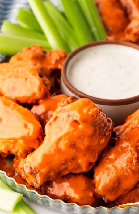 Closeup of buffalo wings coated in sauce with ranch dip on the side and celery sticks in the background