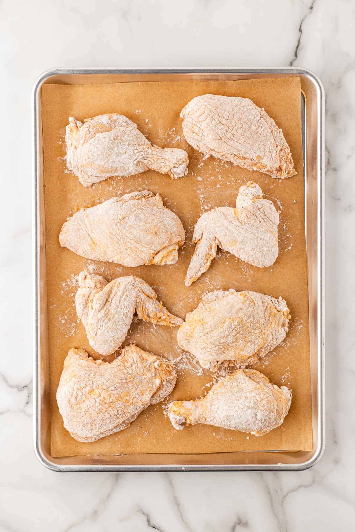 Floured chicken pieces resting on a parchment-lined baking sheet before frying