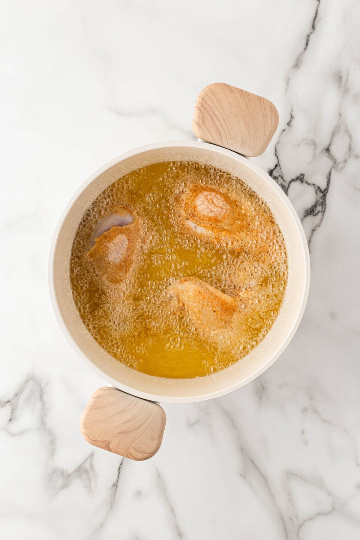 Buttermilk fried chicken pieces frying in bubbling hot oil in a Dutch oven