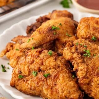 Closeup of crispy buttermilk fried chicken on a white serving platter with parsley garnish