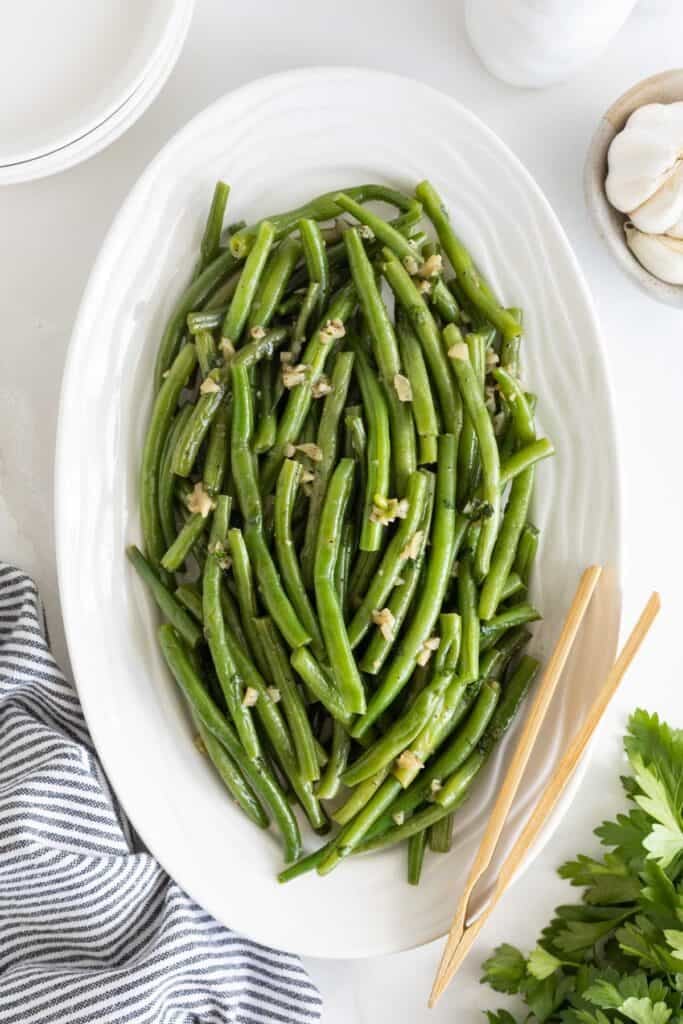 A white platter of garlic green beans ready to serve