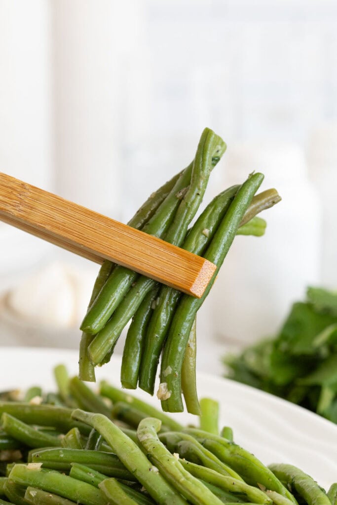 A few garlic green beans being lifted with tongs