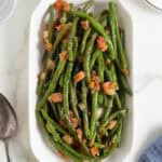 Cooked green beans with tomatoes served in a white oval dish