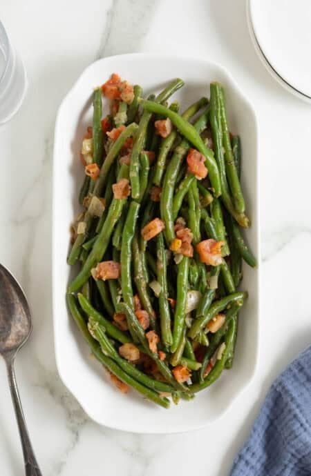 Cooked green beans with tomatoes served in a white oval dish