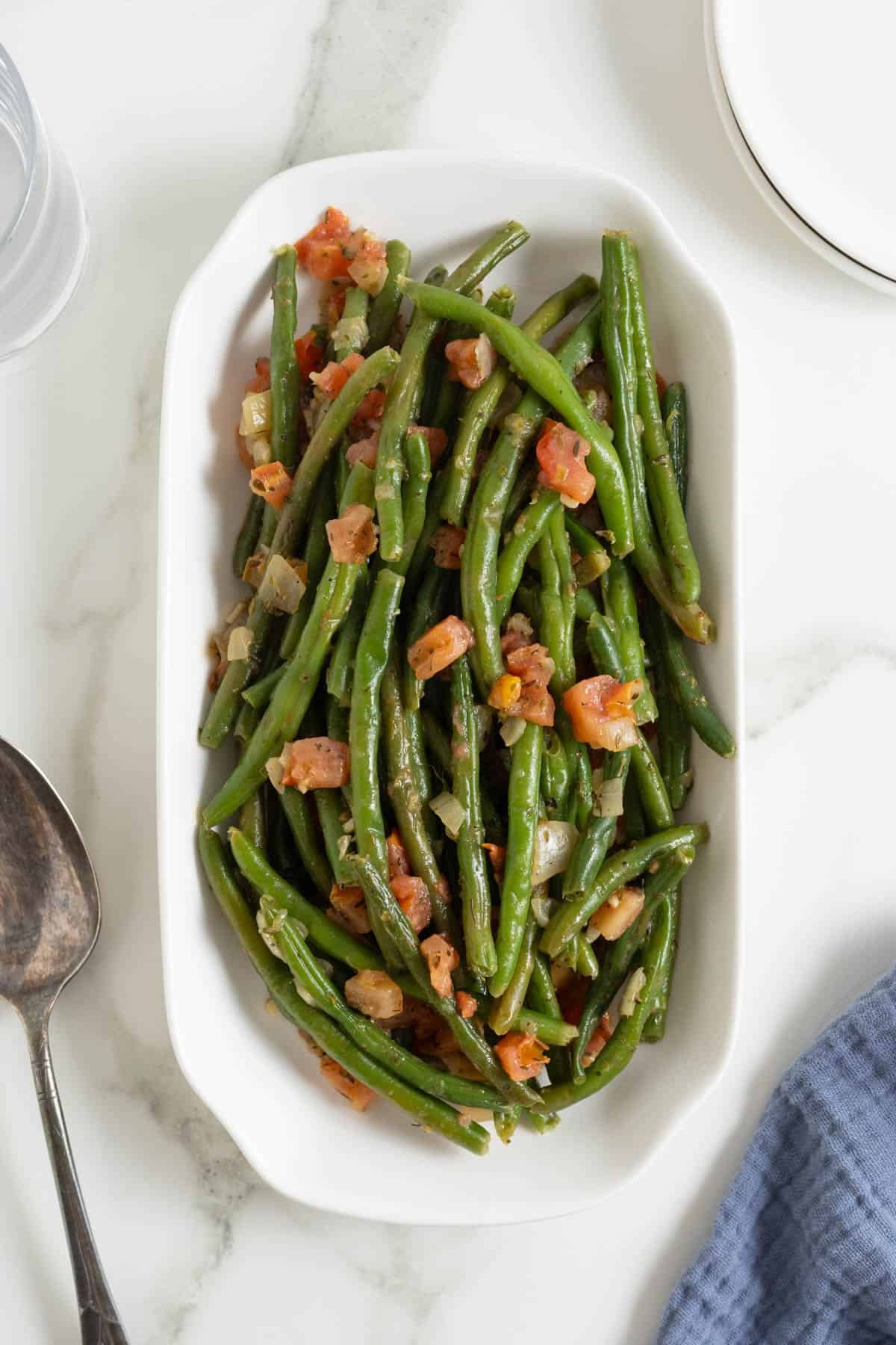 Cooked green beans with tomatoes served in a white oval dish