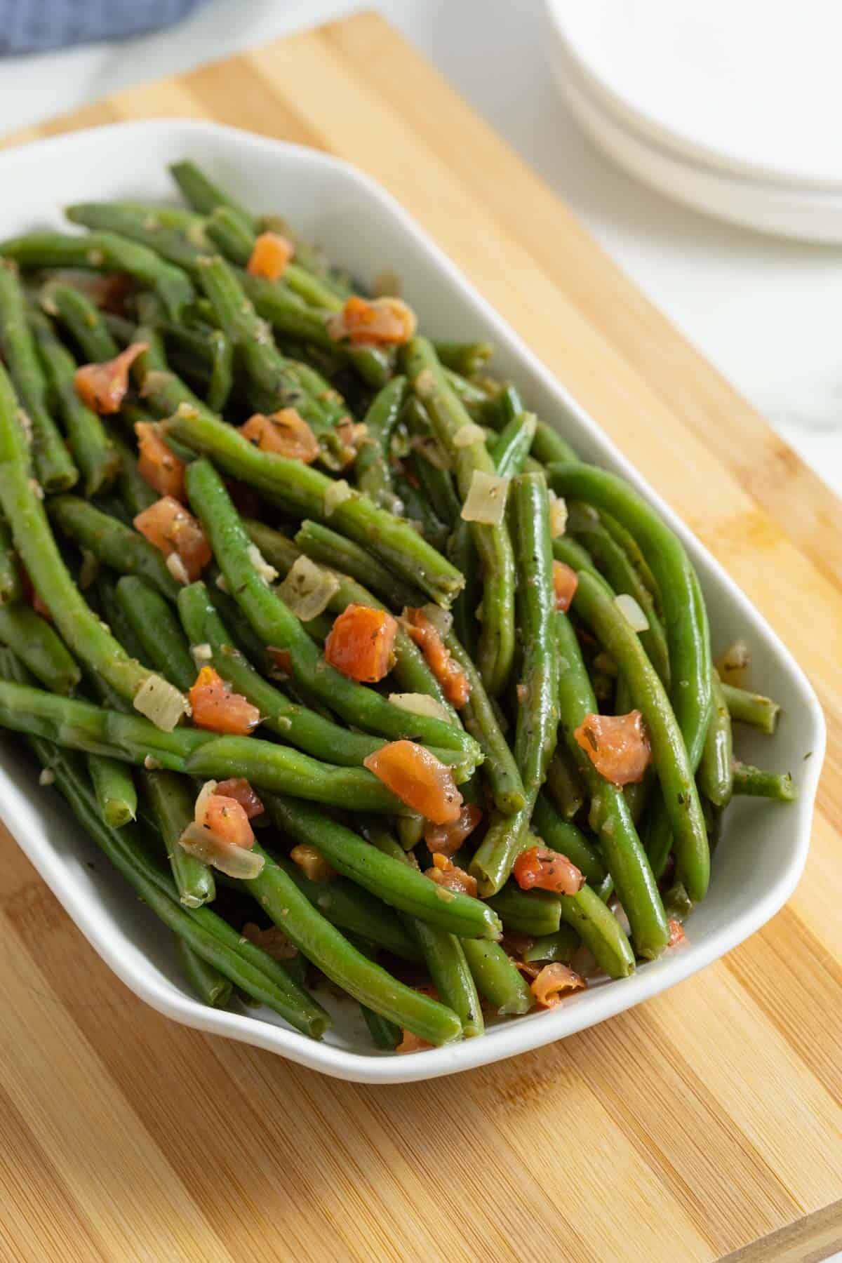 Green beans with tomatoes and onions plated on a white dish placed on a wooden board