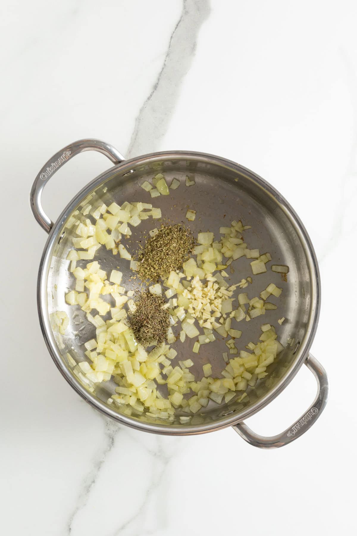 Diced onions, minced garlic, and dried herbs sautéing in olive oil in a skillet