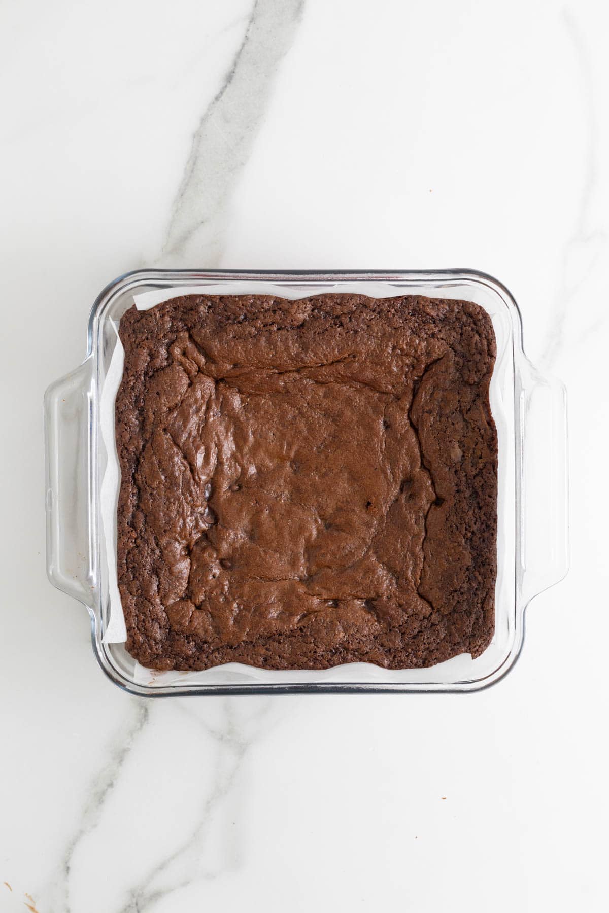 A square pan of freshly baked sweet potato brownies resting in a glass dish lined with parchment paper