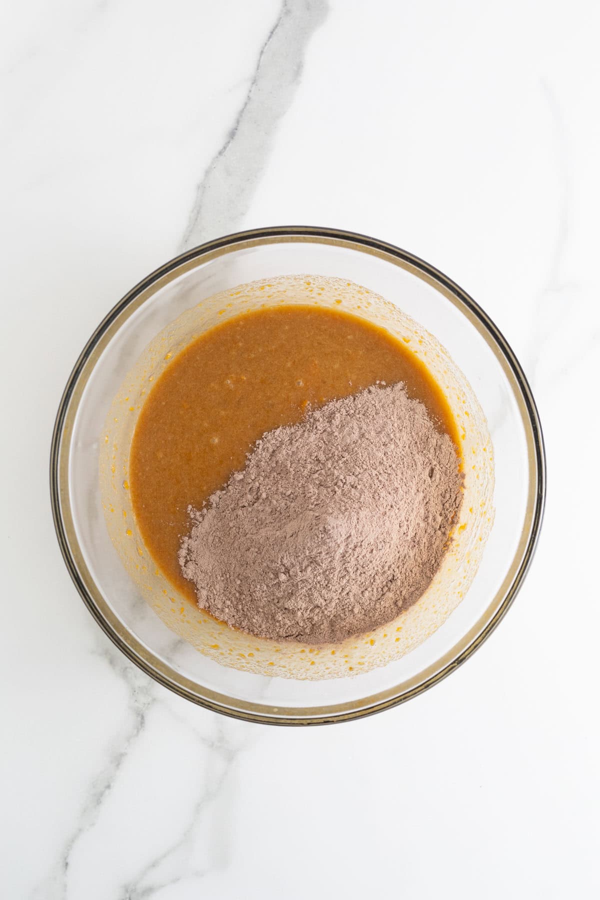 A mixing bowl showing wet ingredients partially combined with the dry cocoa brownie mix, ready to be stirred