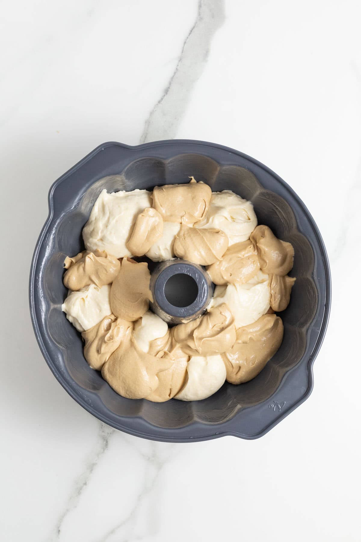 Spoonfuls of pale yellow and brown cake batter placed on top of the cocoa-dusted ladyfingers