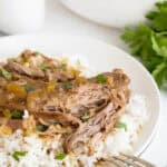 A plate of white rice topped with a turkey neck and smothered in brown gravy with chopped celery and herbs