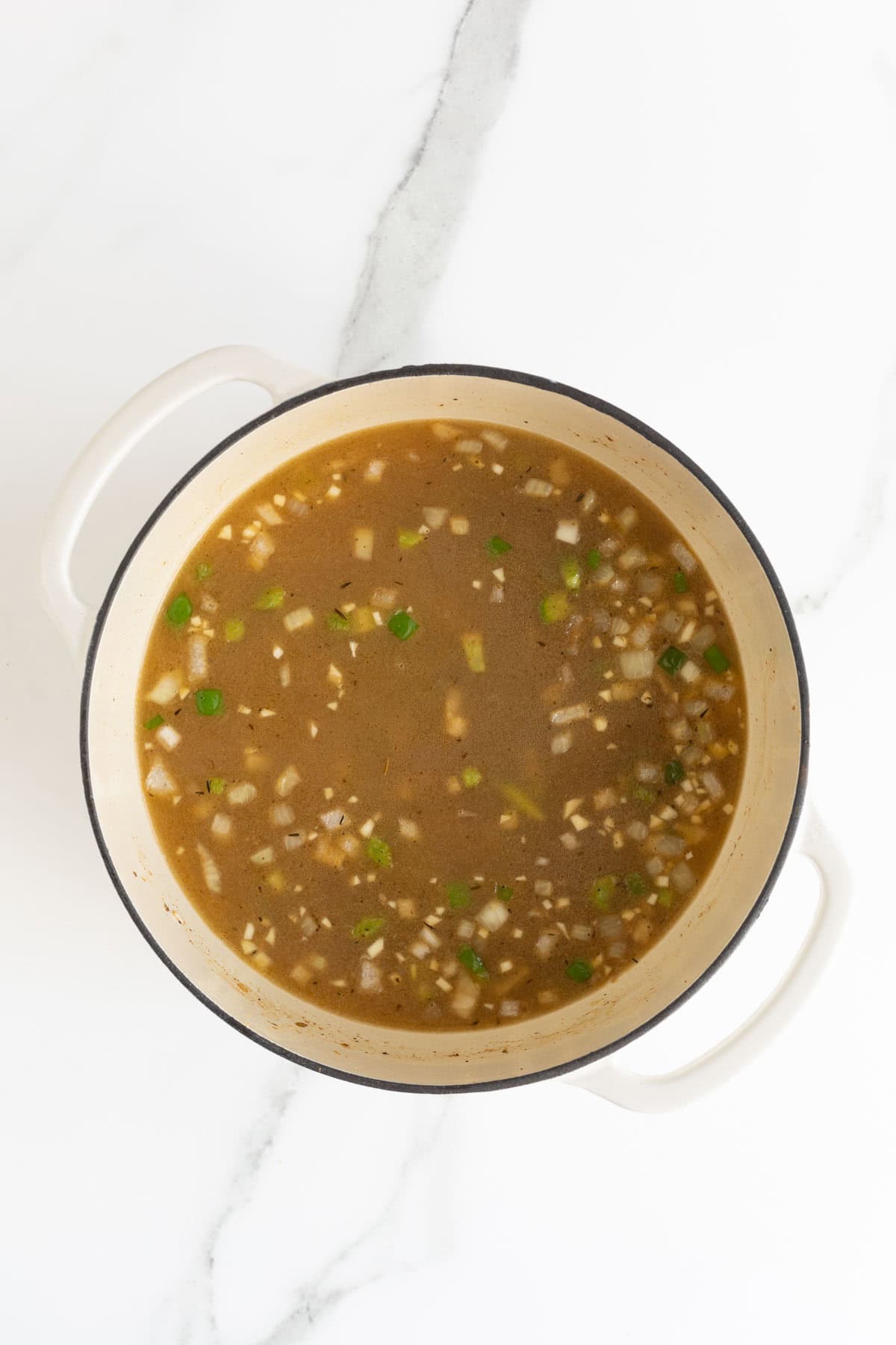 A Dutch oven filled with broth, onions, and green bell peppers simmering together