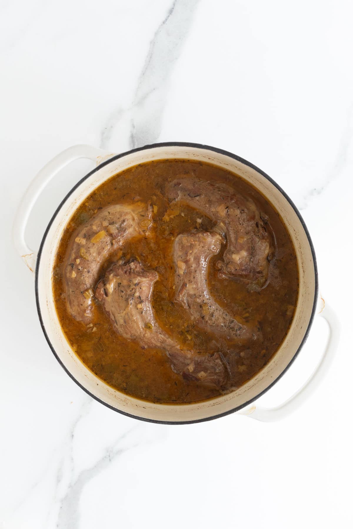 Turkey necks simmering in a flavorful gravy inside a Dutch oven, nearly finished cooking