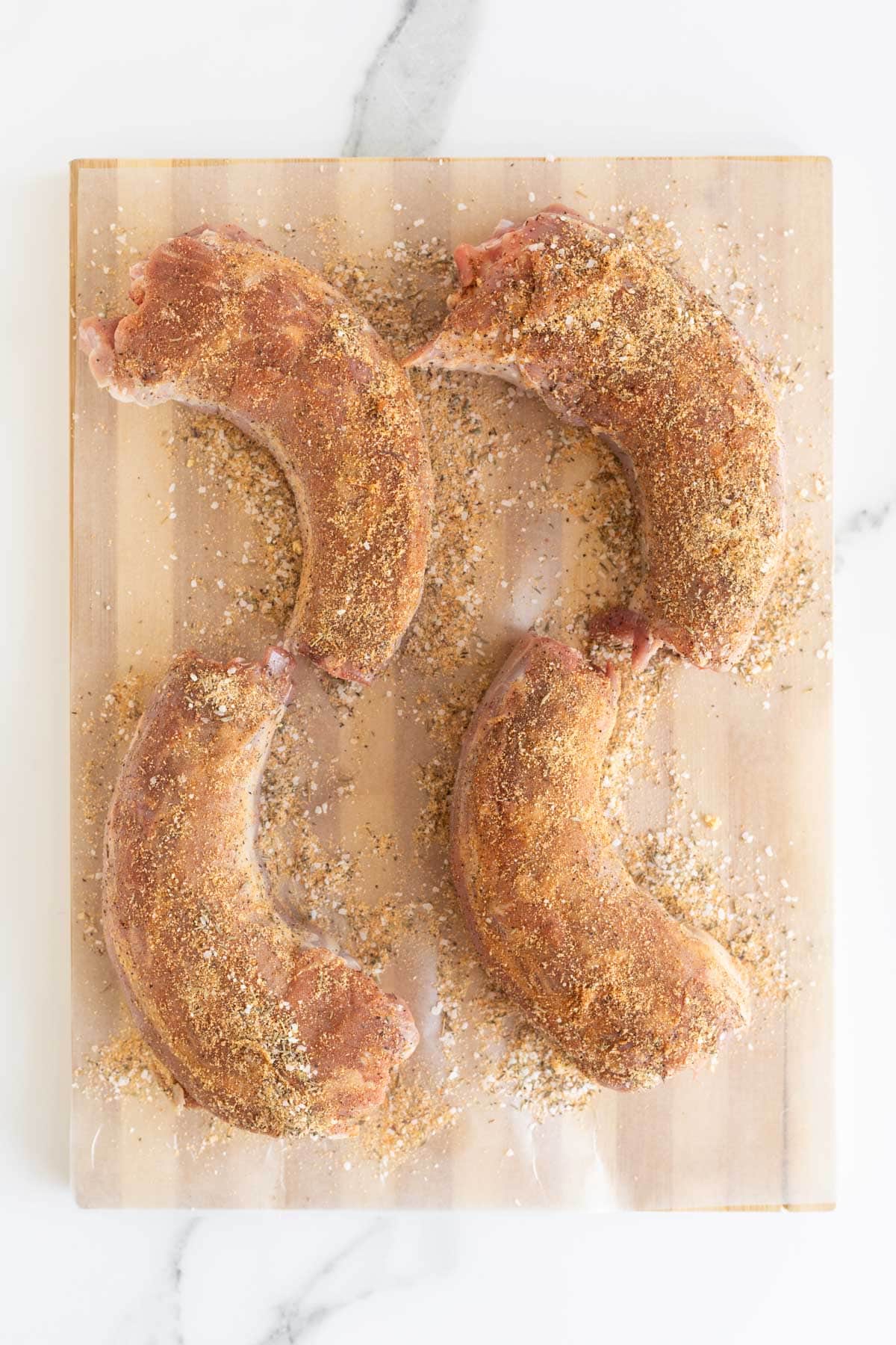 Raw turkey necks coated in seasoning blend on a wooden cutting board