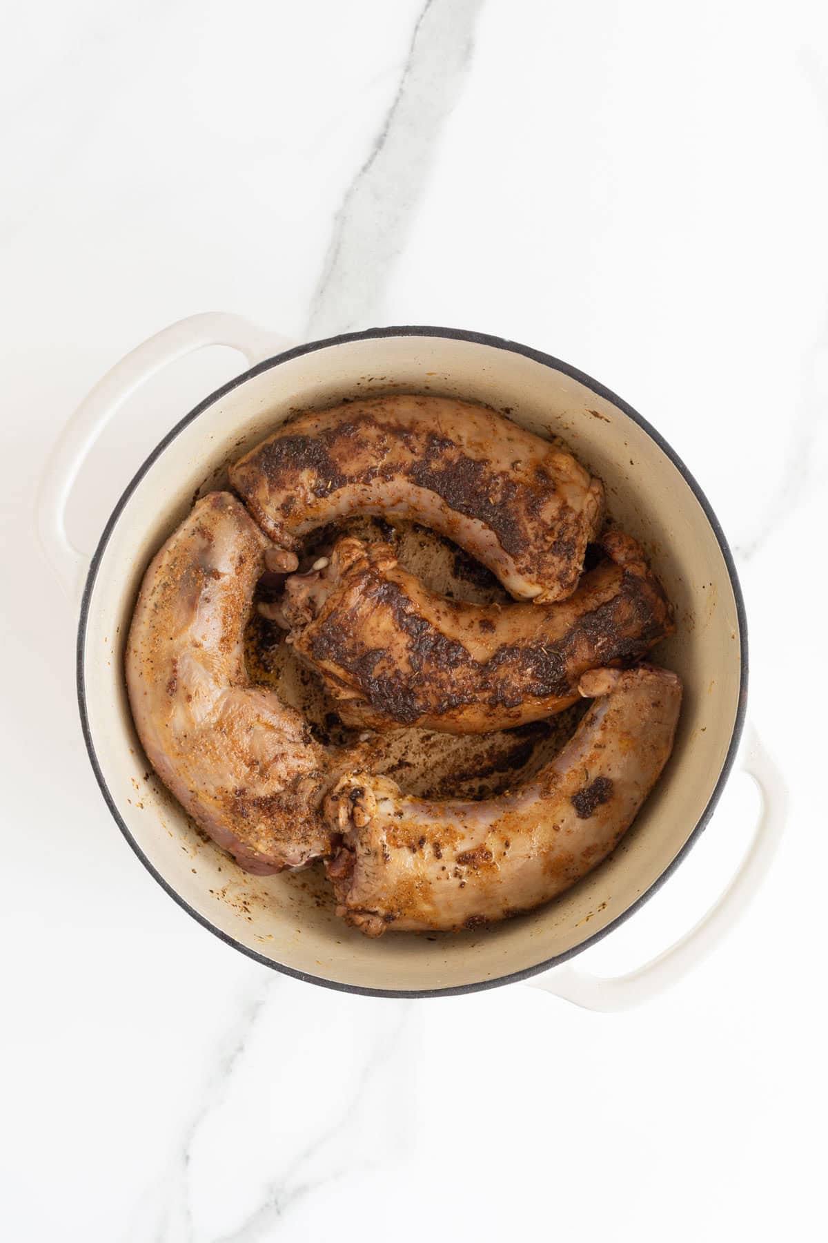 Seasoned turkey necks searing and browning in a large cream-colored Dutch oven