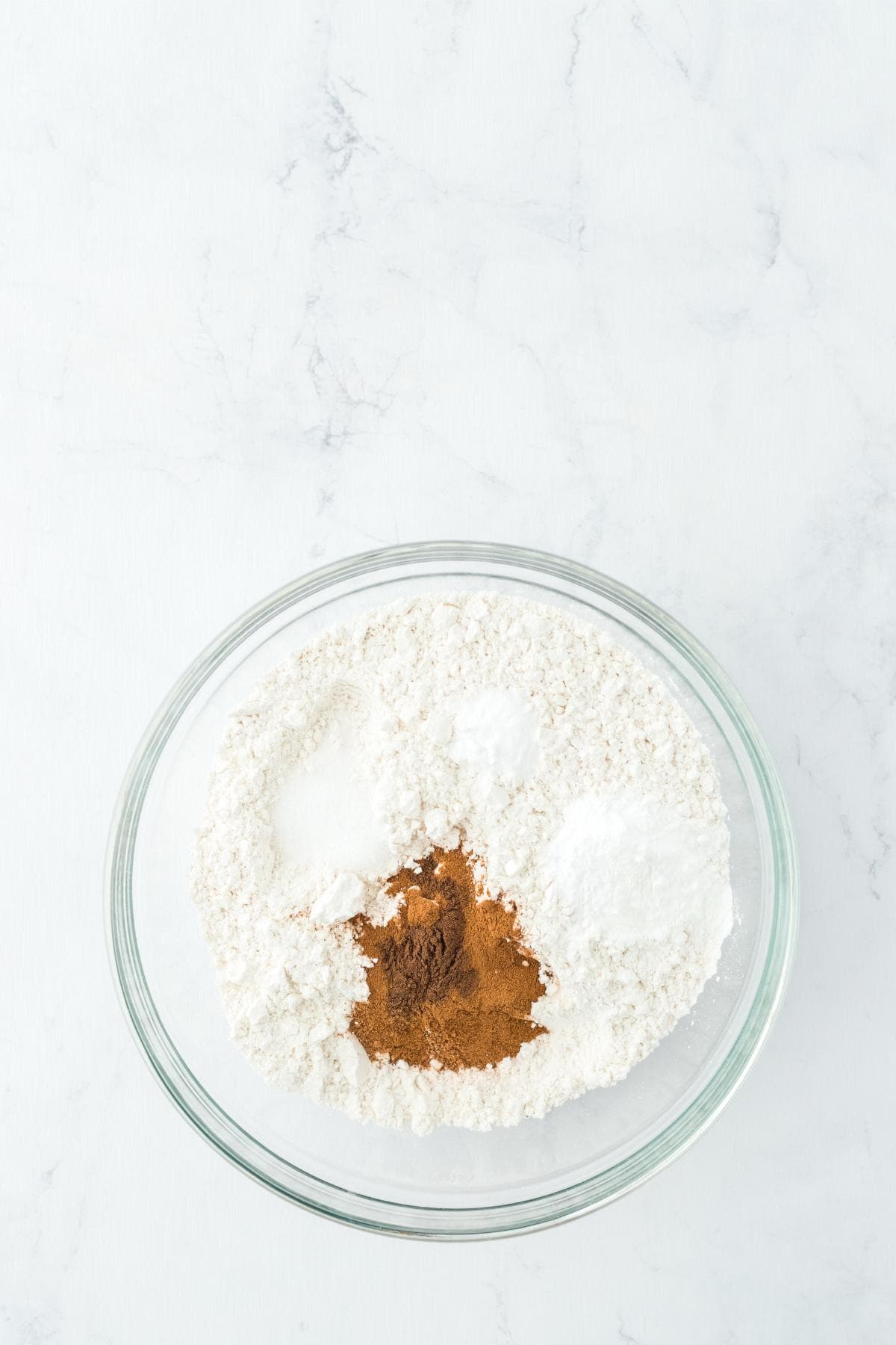 Bowl of flour with sugar, baking powder, and spices on a white surface