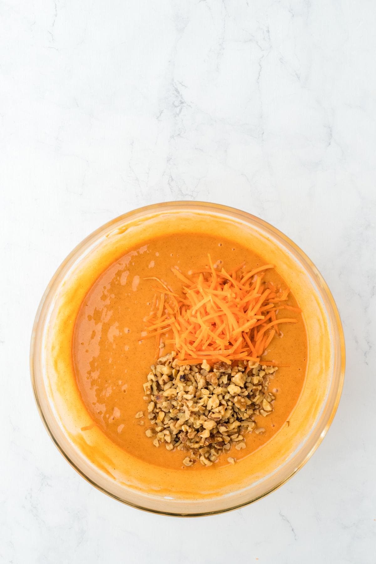 Batter in a bowl topped with shredded carrots and chopped nuts