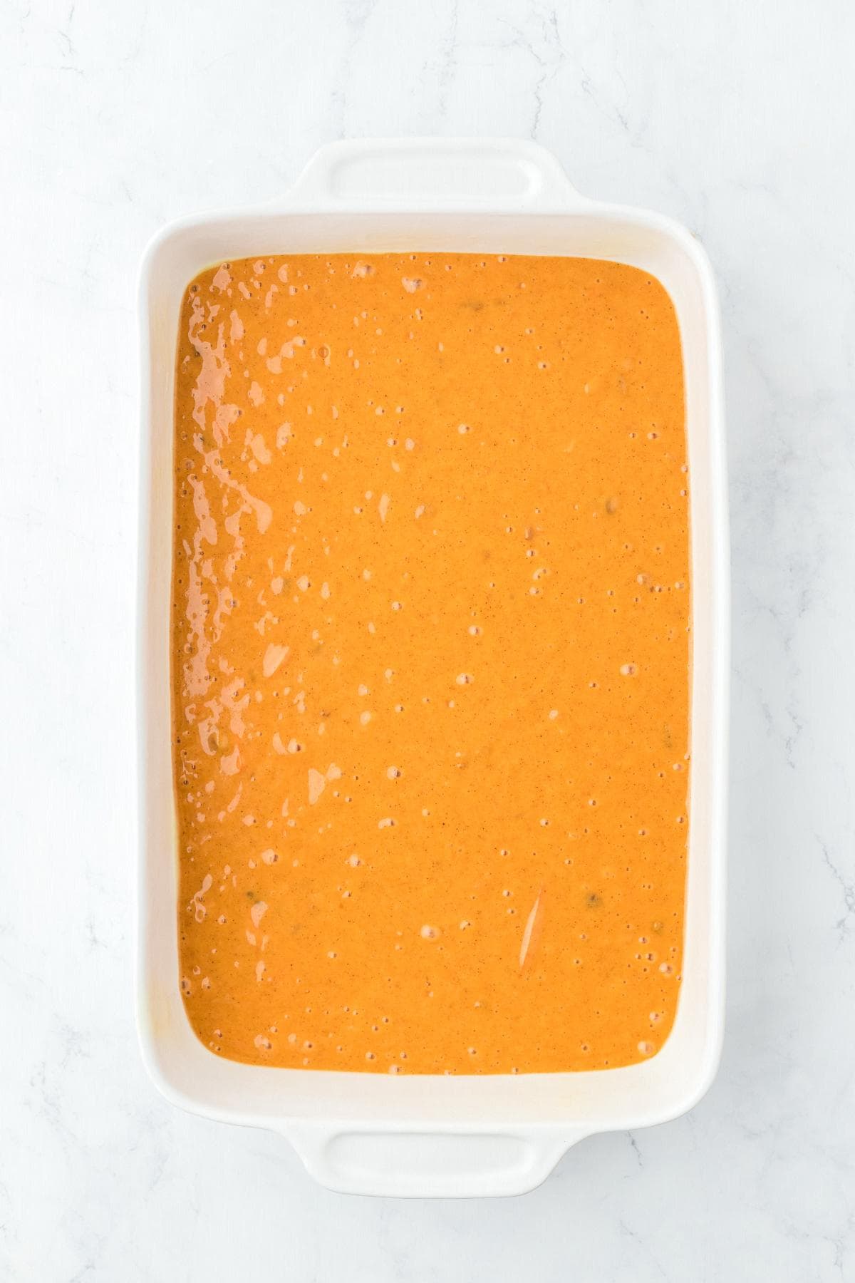 Smooth carrot cake batter poured into a white rectangular baking dish