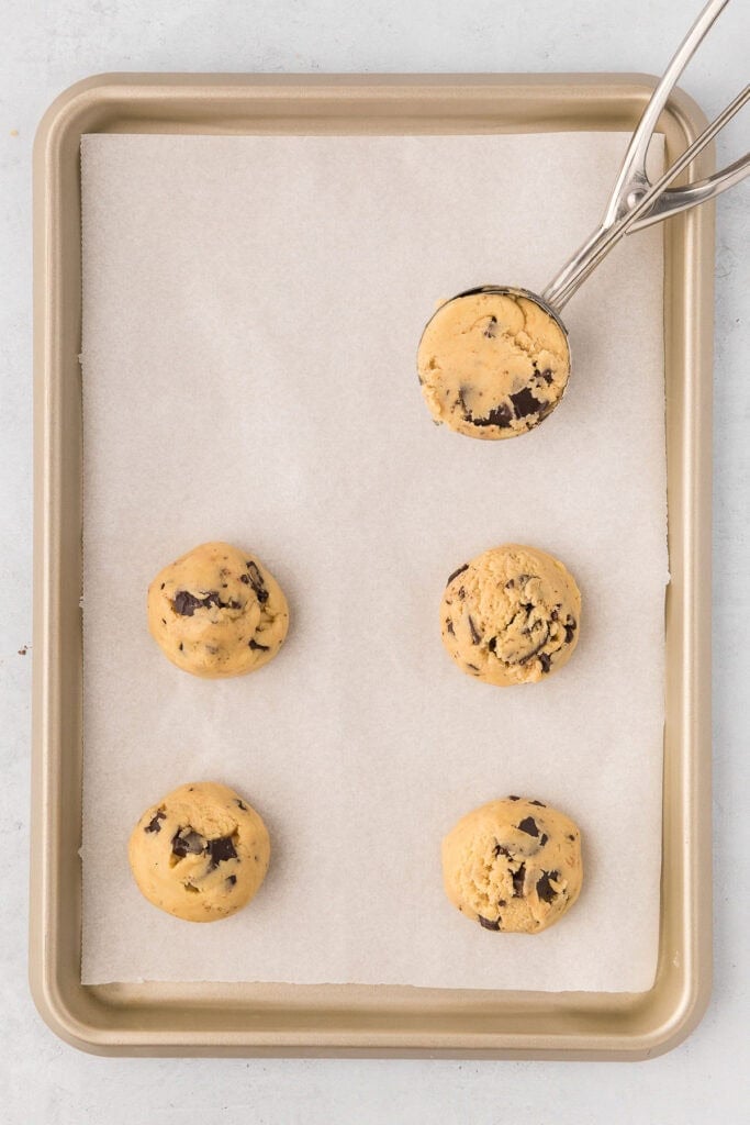 Cookie dough being scooped on parchment paper on cookie sheets