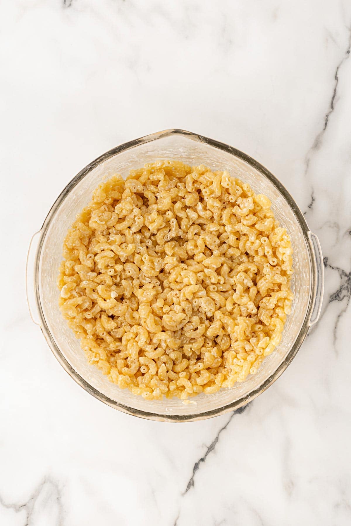 Cooked elbow macaroni mixed with melted butter and cream cheese in a glass bowl