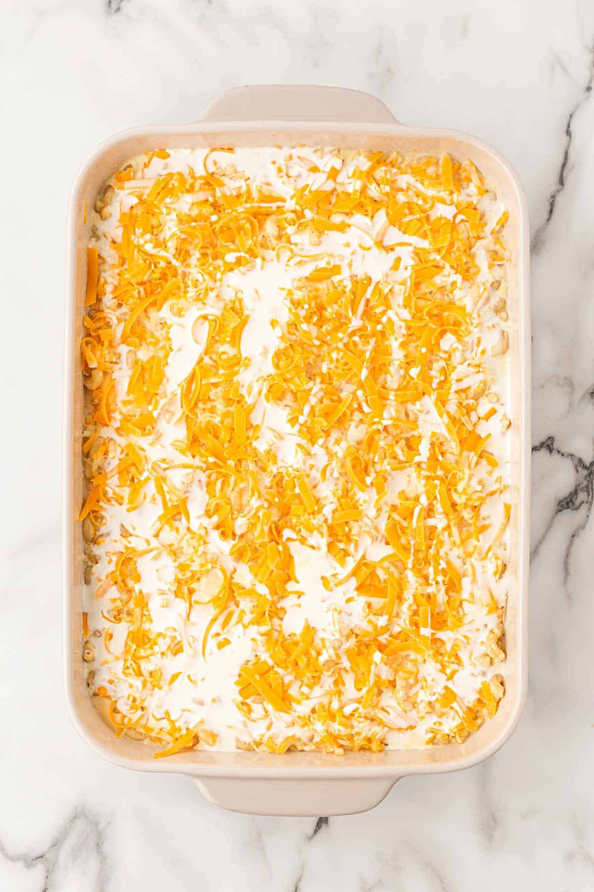 Unbaked mac and cheese topped with shredded cheese and heavy cream in a baking dish