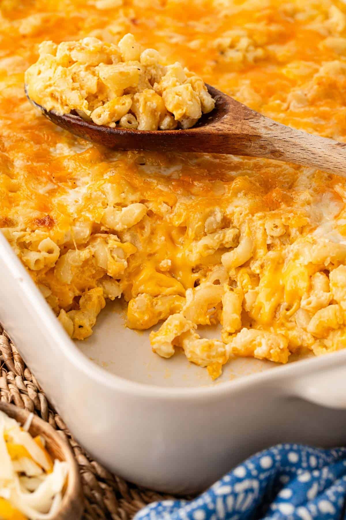 Closeup of creamy baked mac and cheese with eggs being served with a wooden spoon