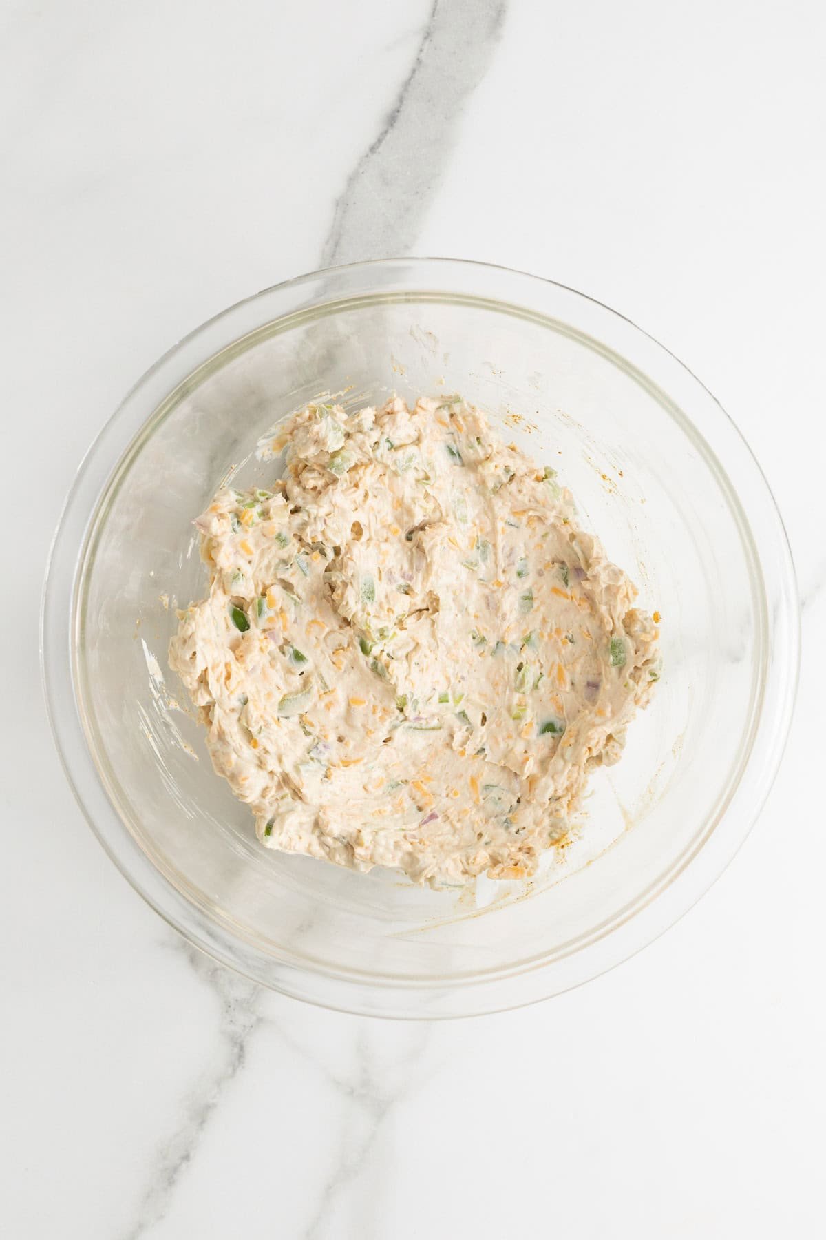 A glass bowl showing the cheese mixture fully combined with the added vegetables and spices