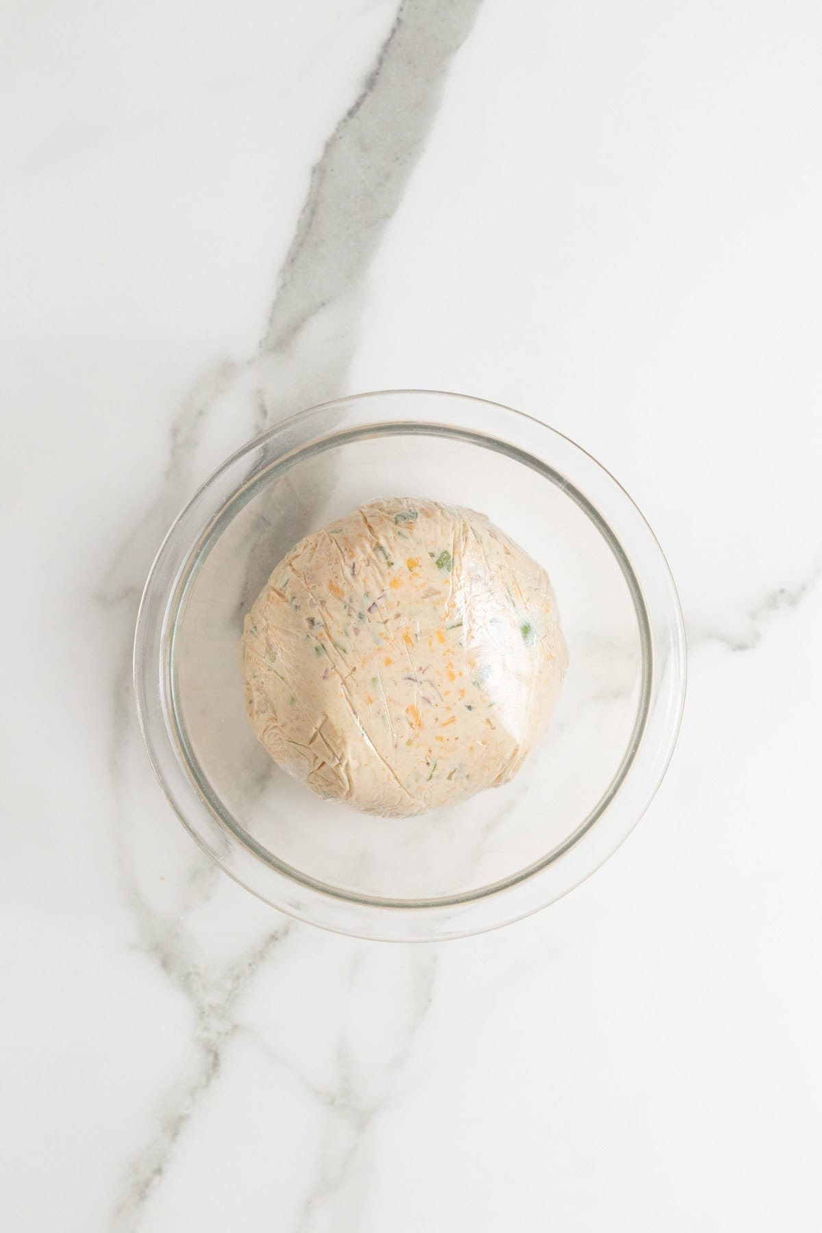 Cheese mixture wrapped tightly in plastic wrap, shaped into a ball