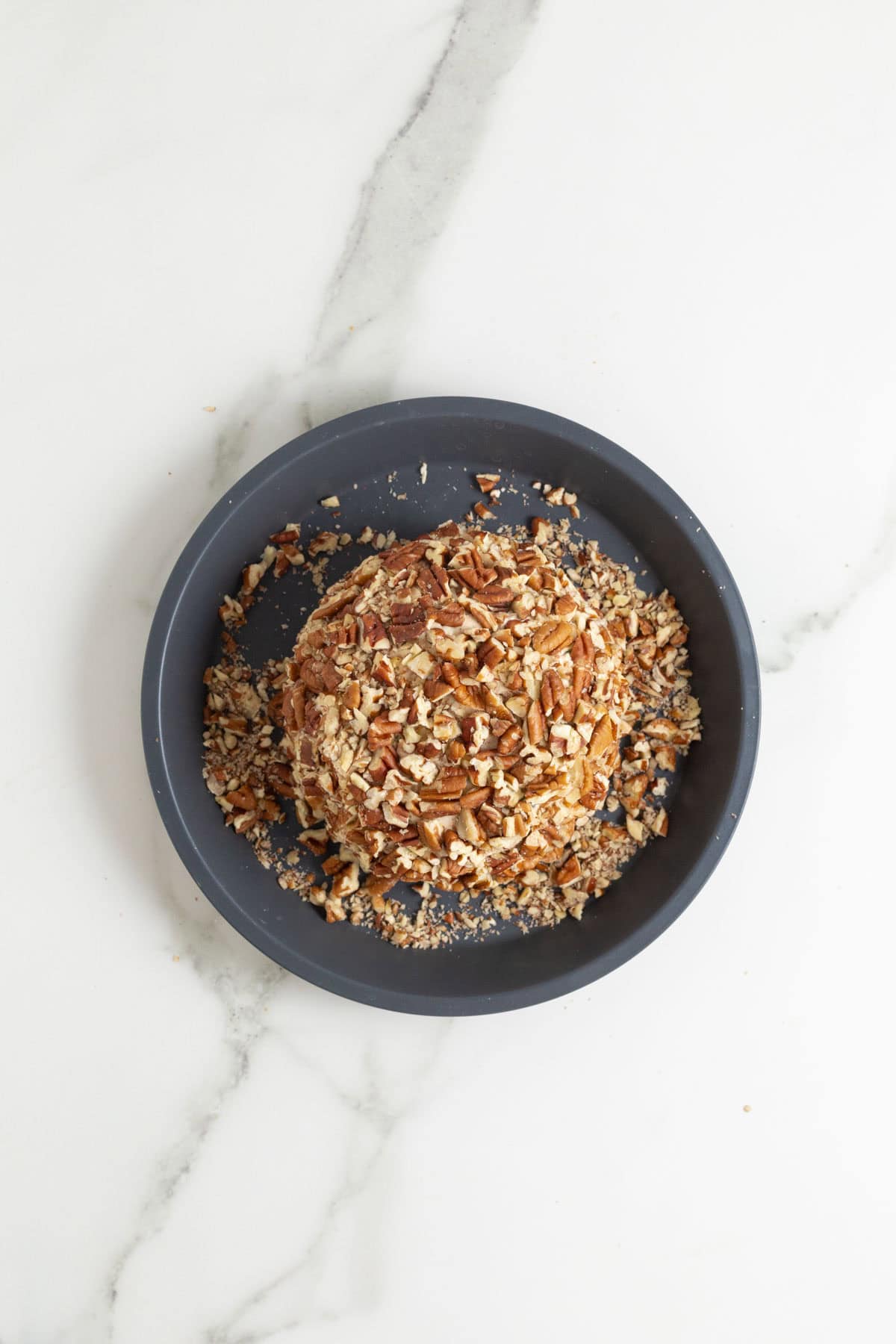 Cheese ball being rolled in chopped pecans on a plate