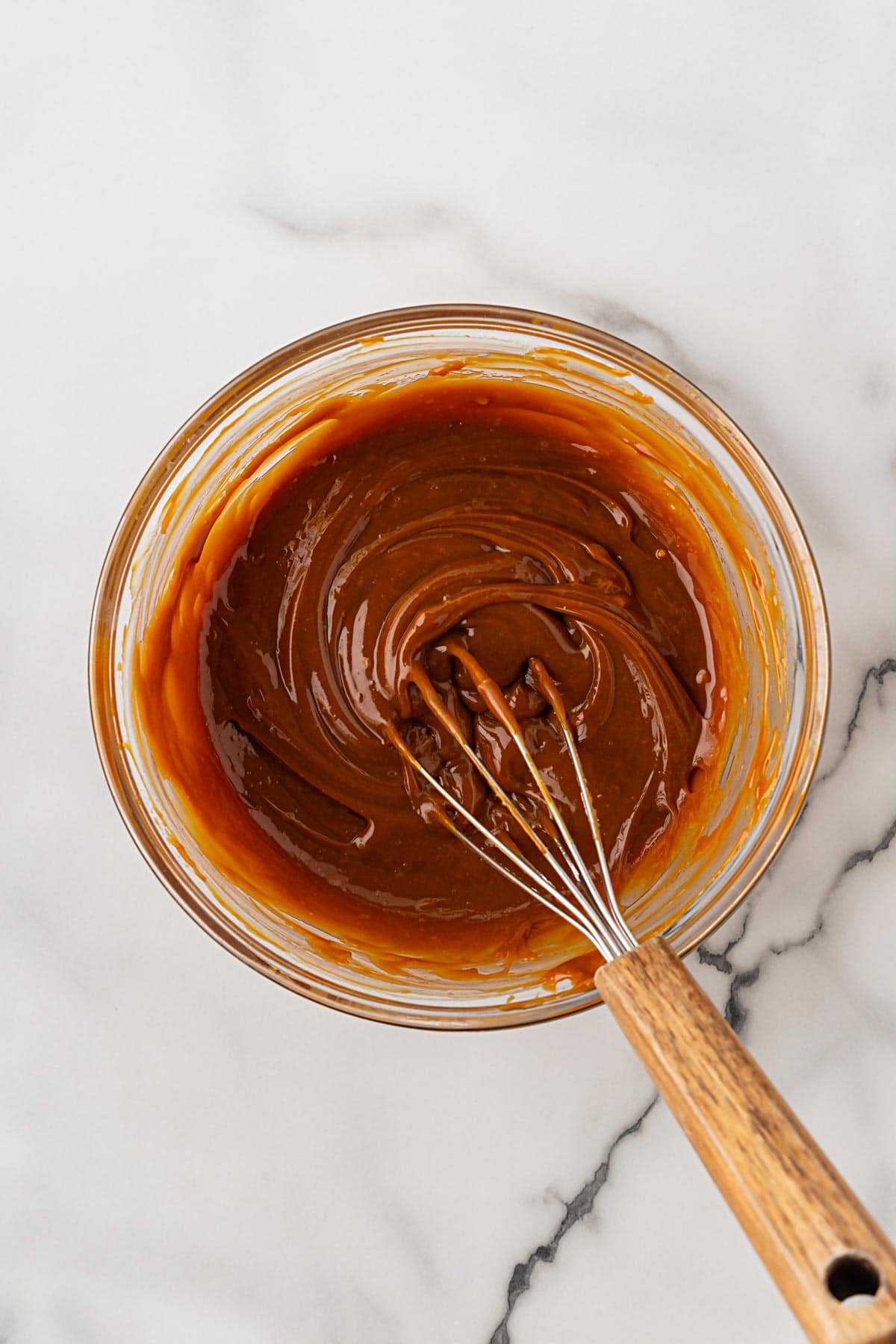 Bowl of thick caramel sauce with a whisk resting inside