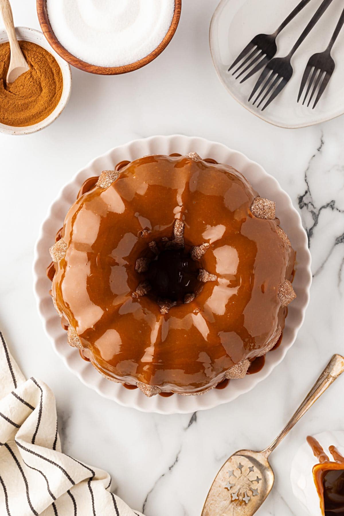 Overhead view of churro pound cake topped with dulce de leche glaze, surrounded by bowls of sugar and cinnamon