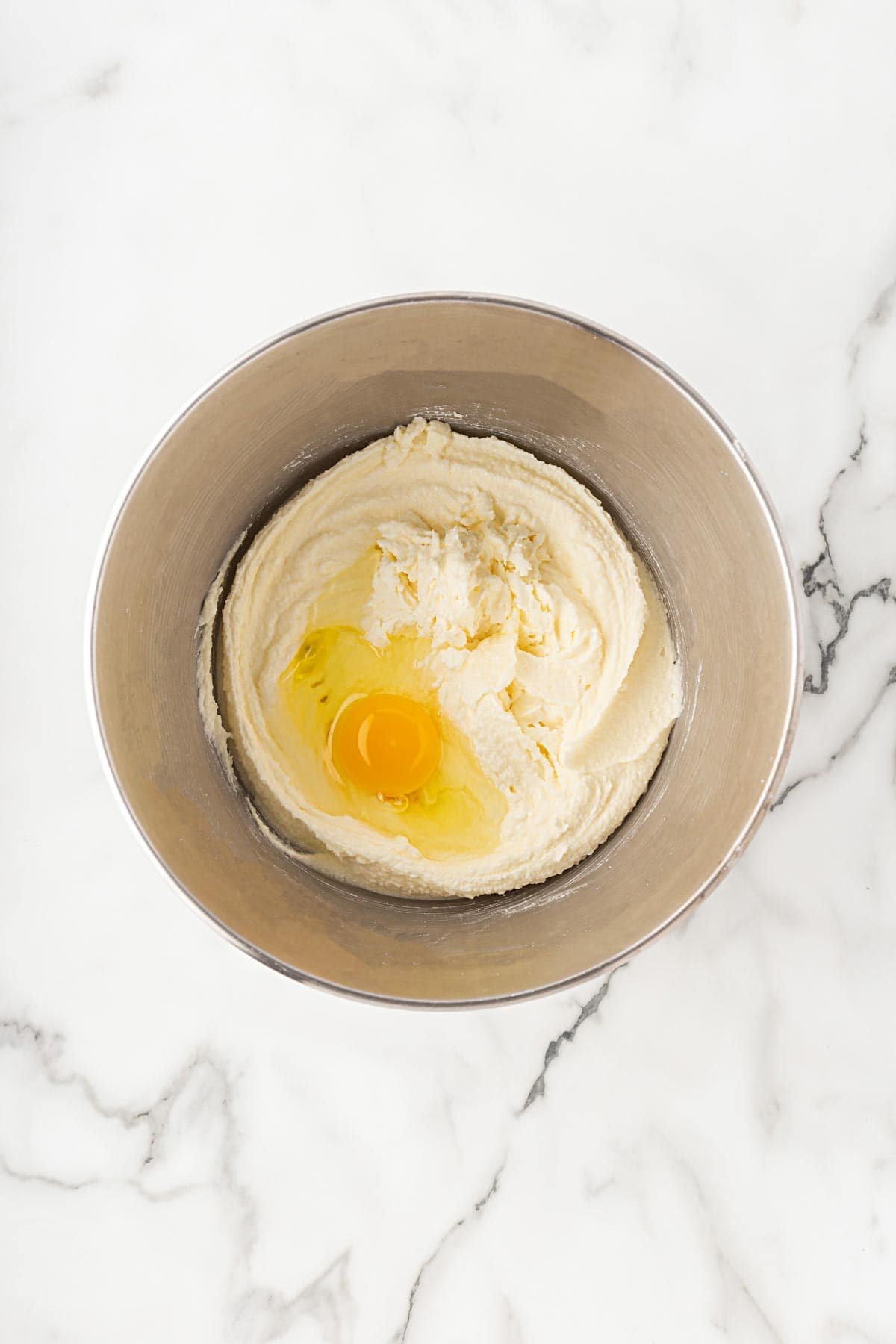 Mixing bowl with creamed butter and sugar topped with a raw egg
