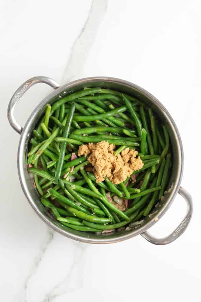 Brown sugar and balsamic added to green beans and bacon in a skillet