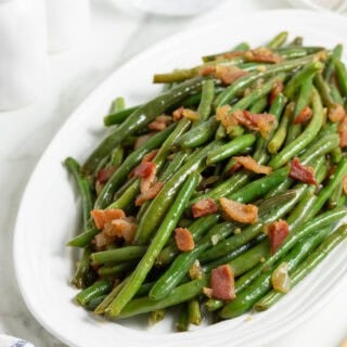 A large white platter of green beans with bacon recipe