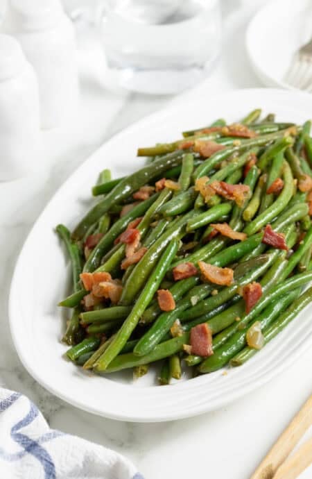 A large white platter of green beans with bacon recipe