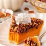 Slice of sweet potato pecan pie topped with whipped cream on a white plate, with a fork holding a bite and pecans scattered nearby