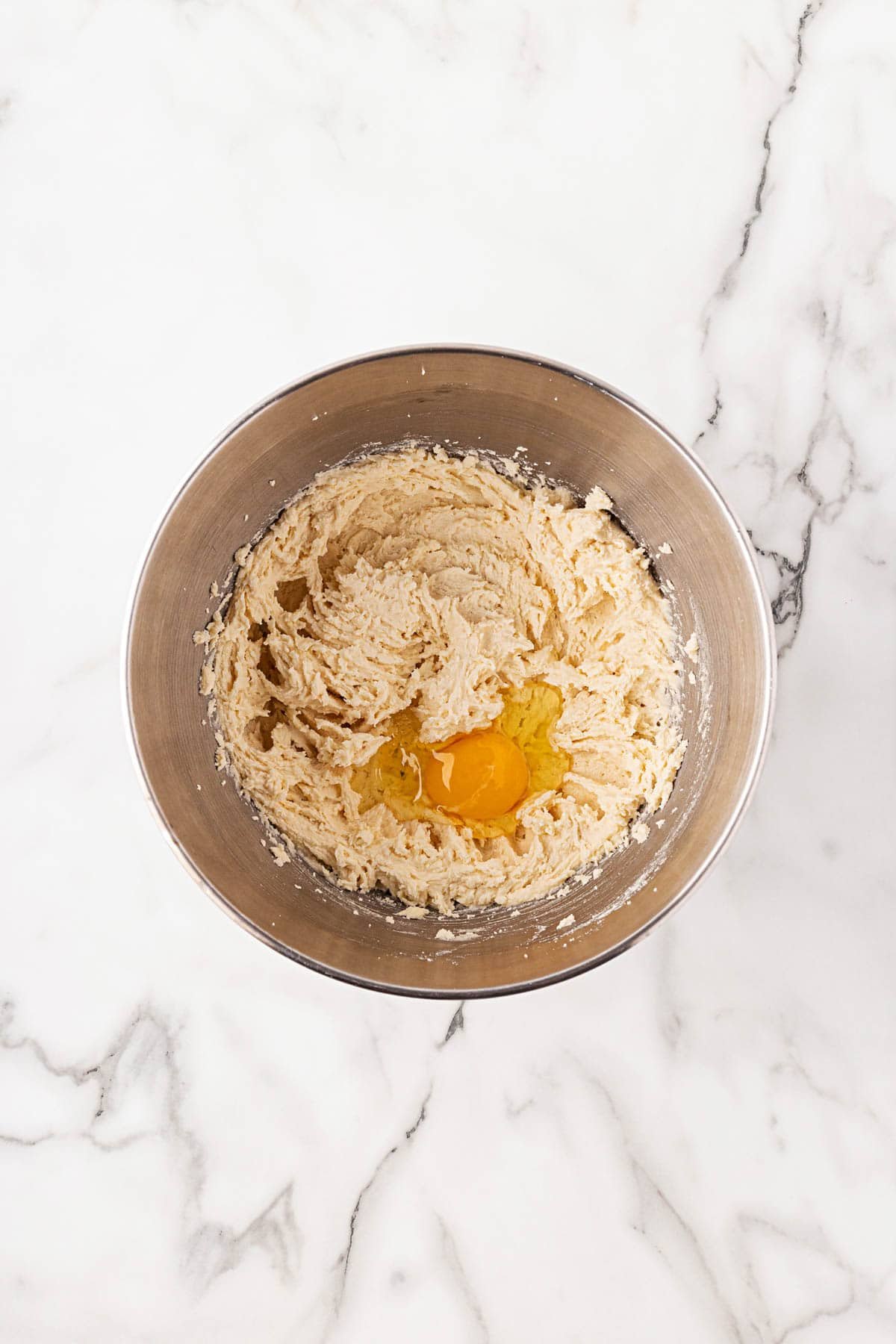 Mixing bowl filled with creamed butter and sugar mixture with an egg cracked in the center, ready to be blended