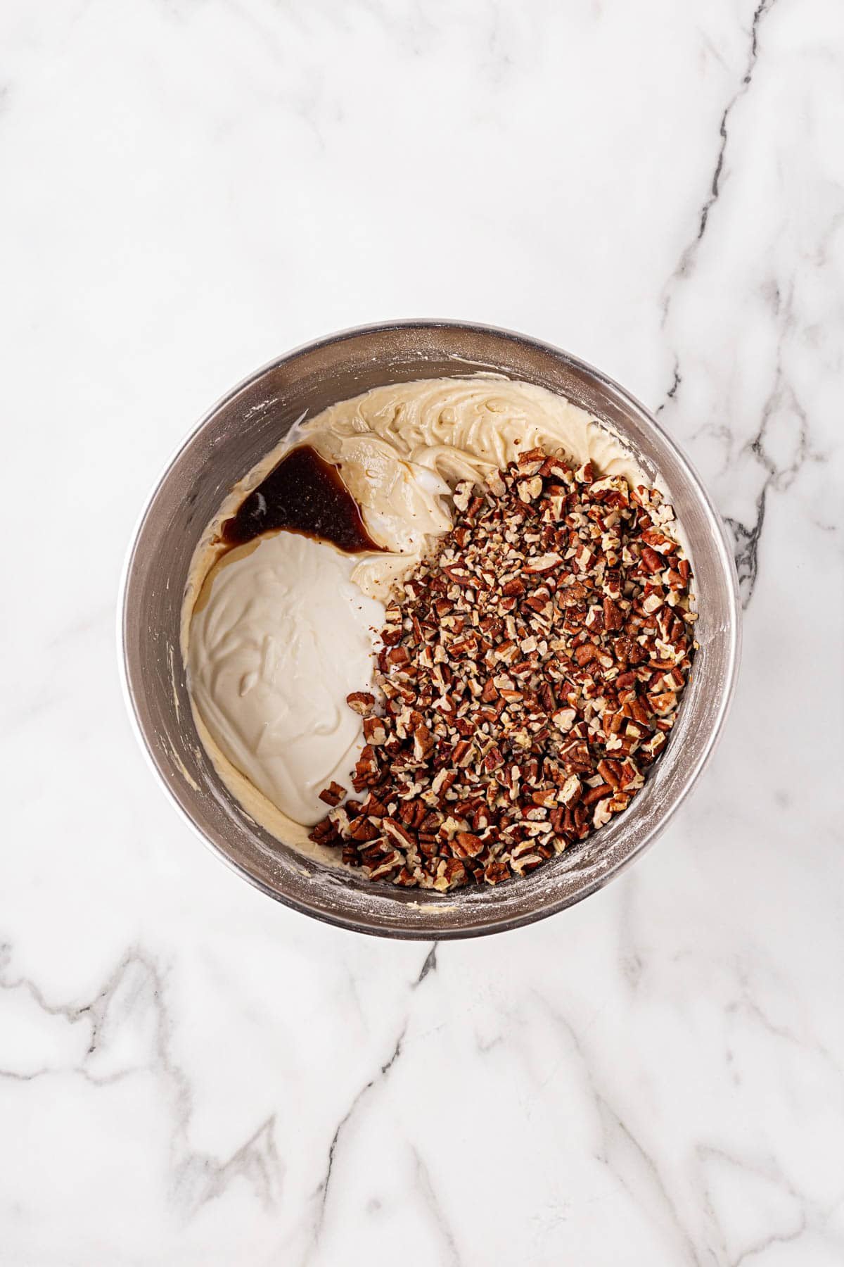 Mixing bowl showing batter with sour cream, toasted pecans, and vanilla added, ready to be folded in