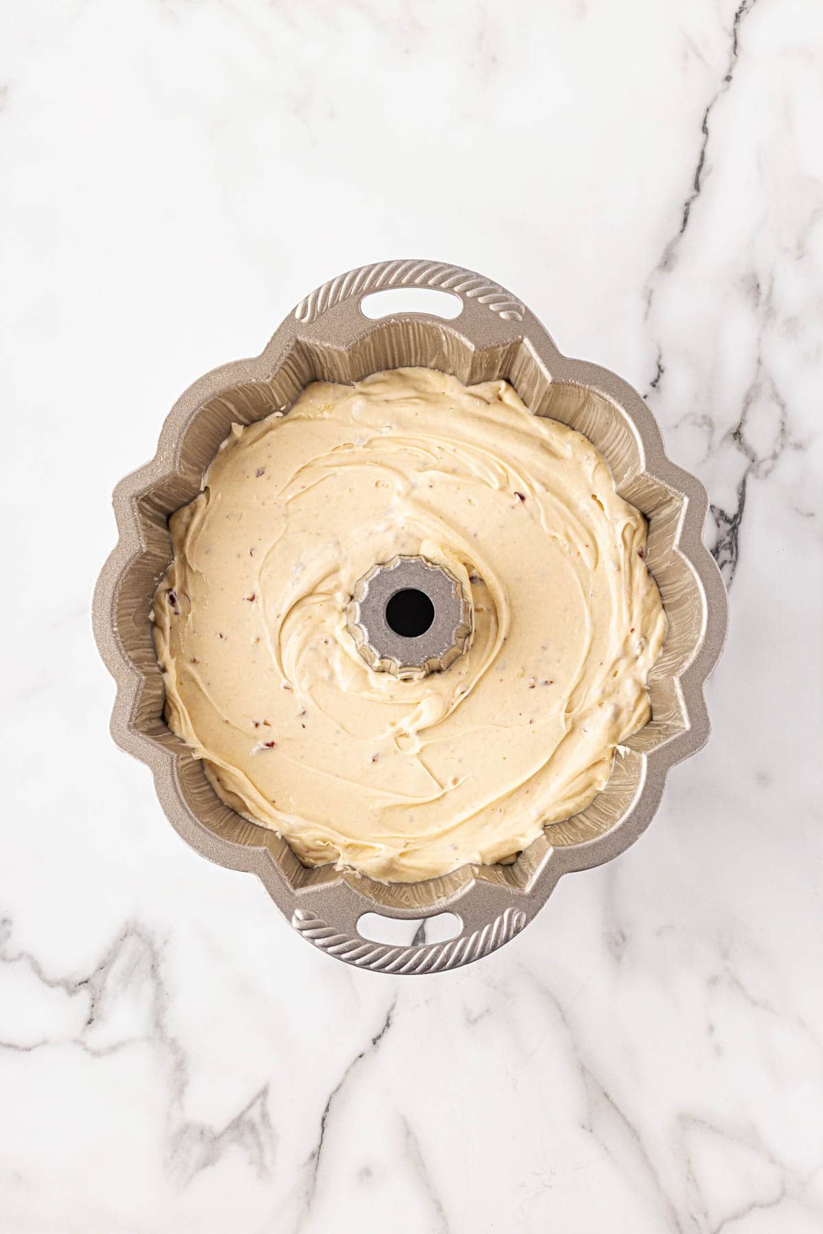 Bundt pan filled with butter pecan pound cake batter, evenly spread and ready for baking