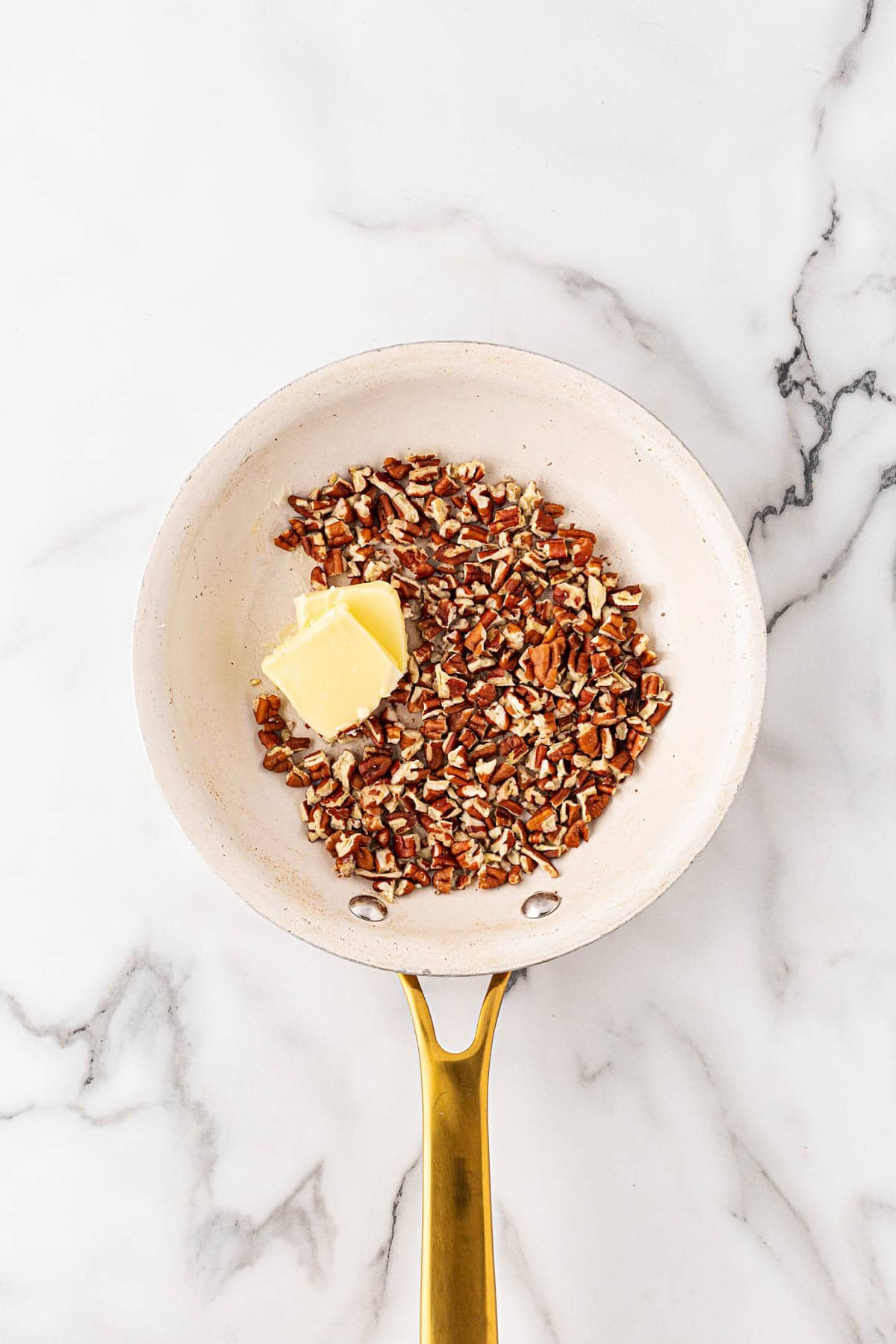 White skillet with chopped pecans and butter melting together to toast