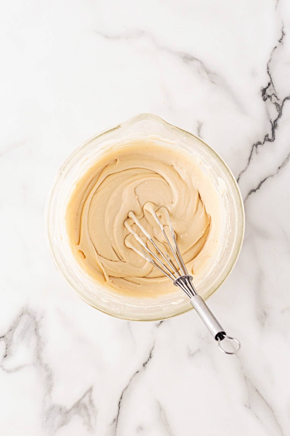 Bowl of butter pecan icing being whisked until smooth on a marble counter