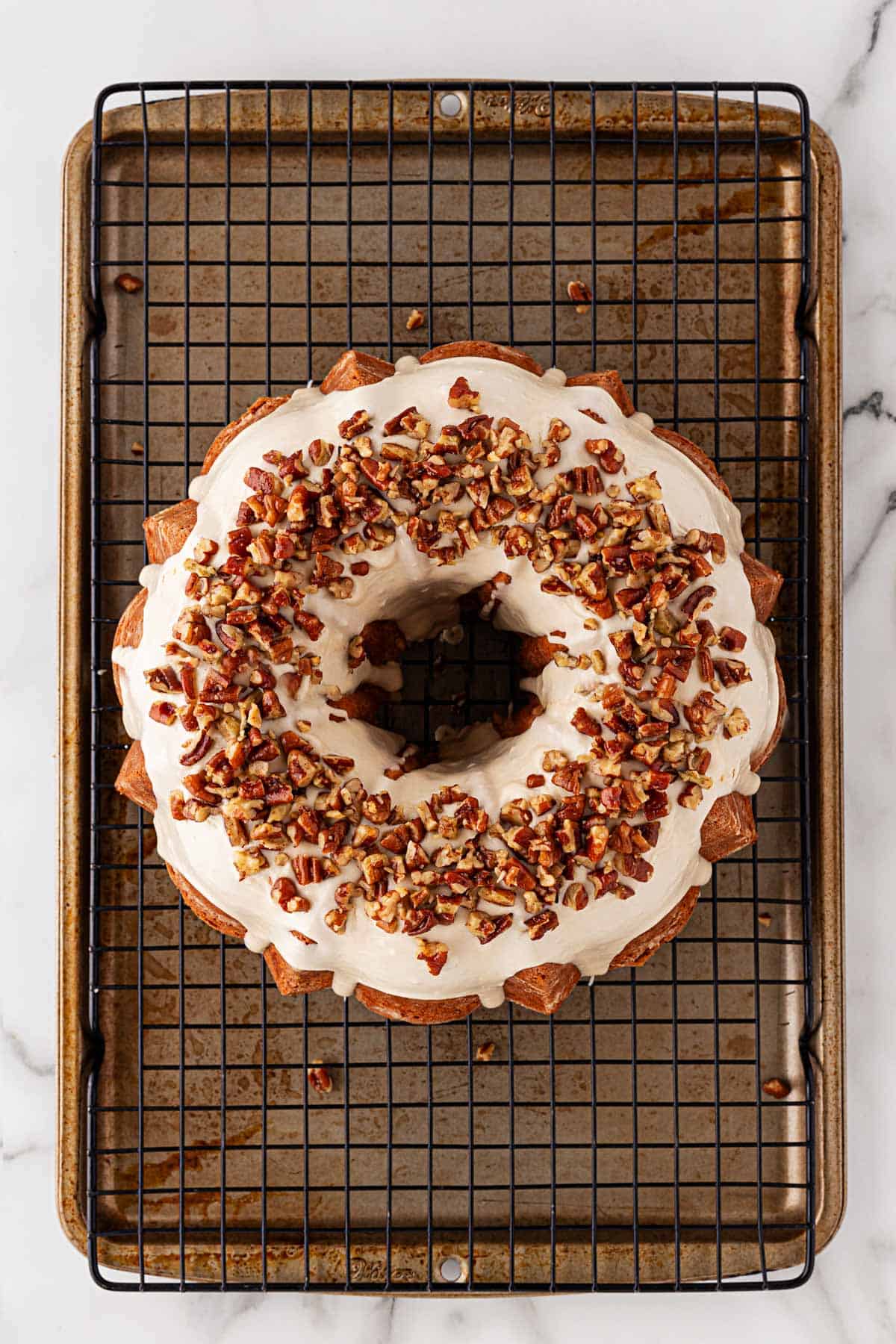 Finished butter pecan pound cake topped with thick glaze and a generous layer of chopped toasted pecans, cooling on a wire rack