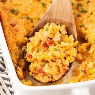 Closeup of a wooden spoon scooping a portion of baked cornbread pudding from a casserole dish