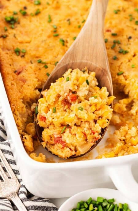 Closeup of a wooden spoon scooping a portion of baked cornbread pudding from a casserole dish