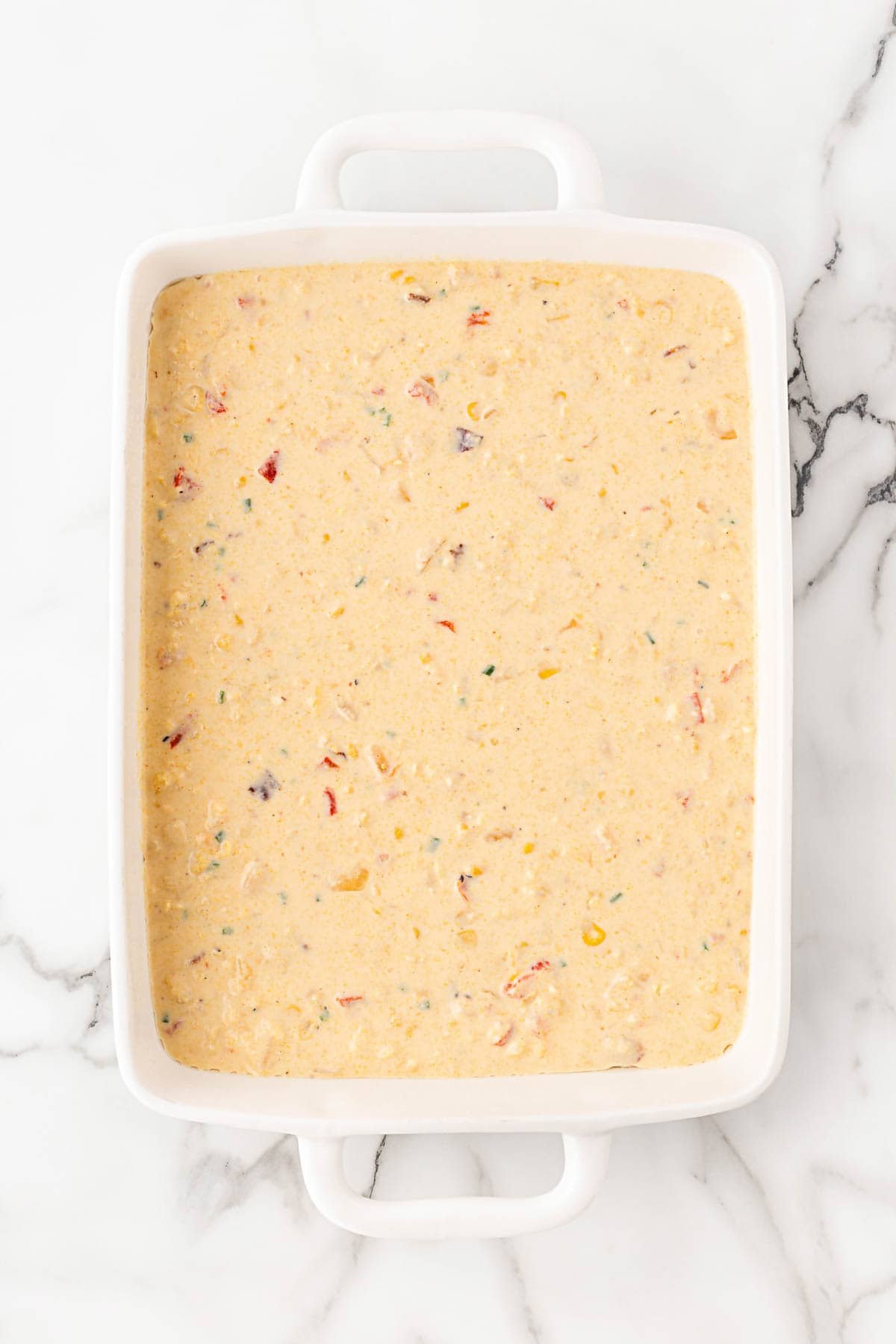 Unbaked cornbread pudding mixture poured evenly into a white rectangular baking dish